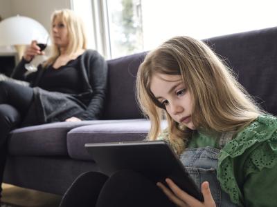 pige med ipad og mor med vinglas i baggrunden
